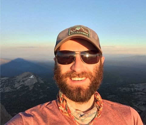 A photo of a man wearing sunglasses standing on top of a mountain